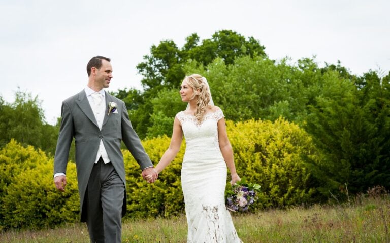 Bride and groom walking hand in hand through a meadow