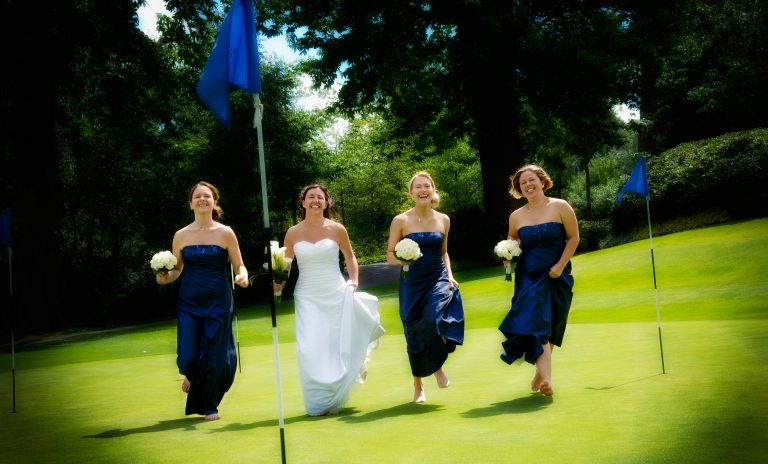 Bride and bridesmaids running across the green at Wentworth Club