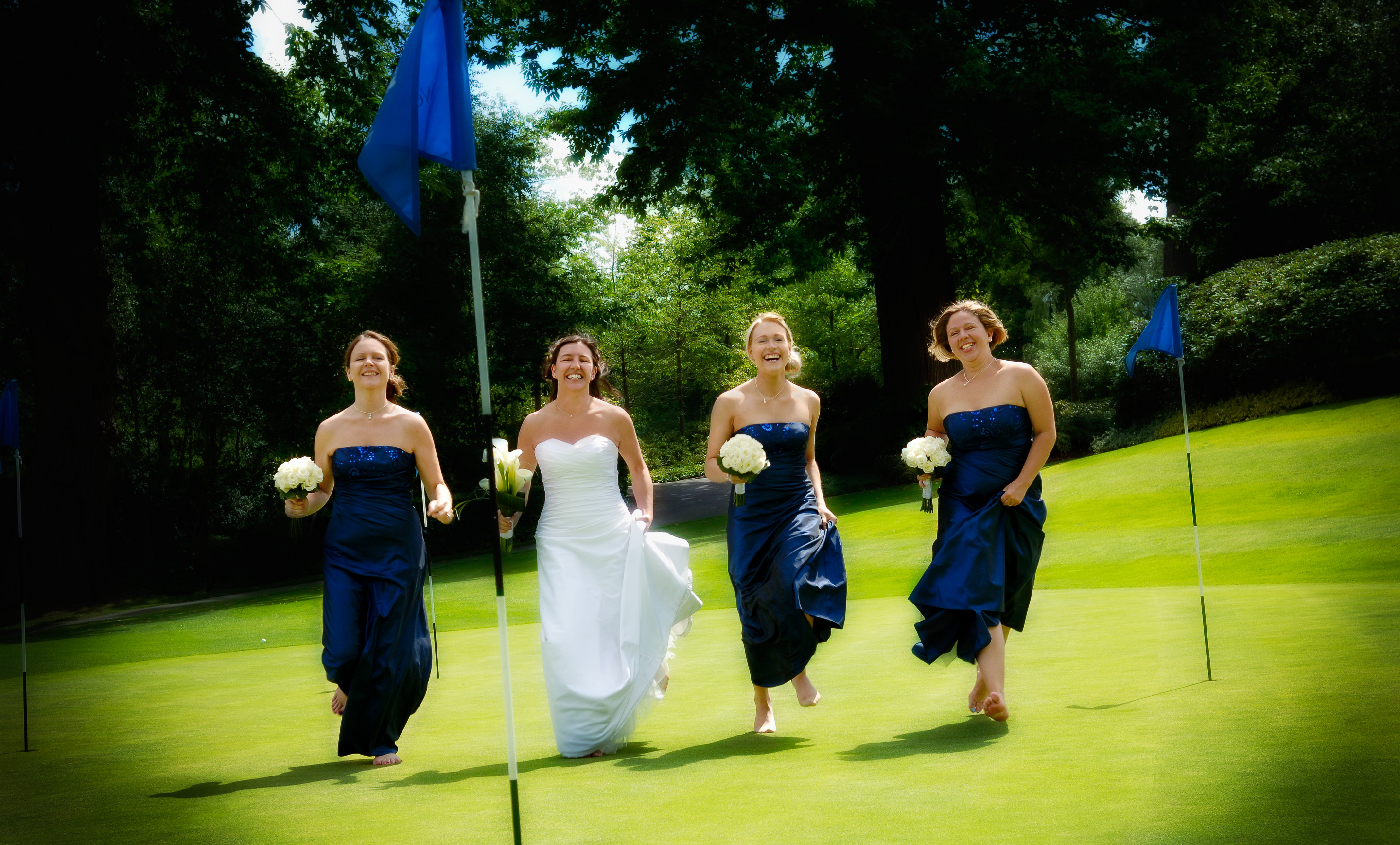 Bride and bridesmaids running across the green at Wentworth Club