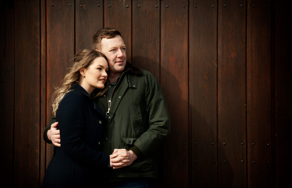 Young couple holding hands leaning against a wood door