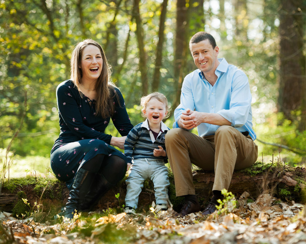 Family of 3 sitting on a log in woodland